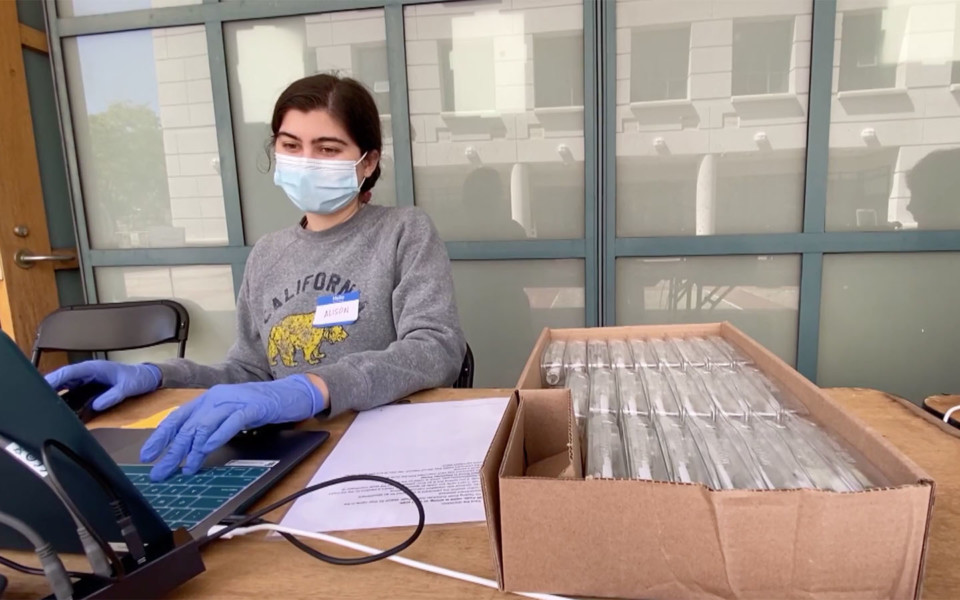 Image of Innovative Genomics Institute volunteer next to a box of COVID-19 saliva tests